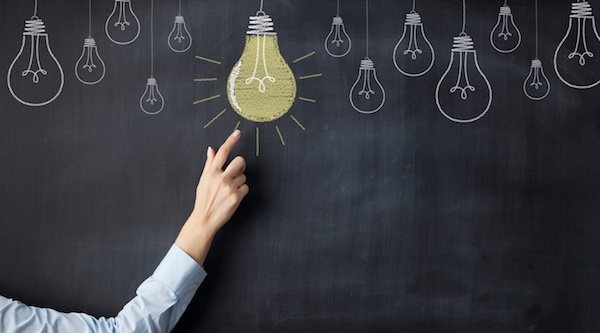 person pointing to a chalkboard drawing of a lightbulb